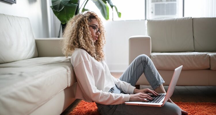 woman sitting on floor and leaning on couch using laptop