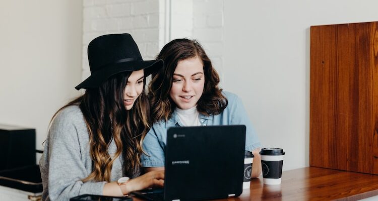 two woman sitting near table using Samsung laptop