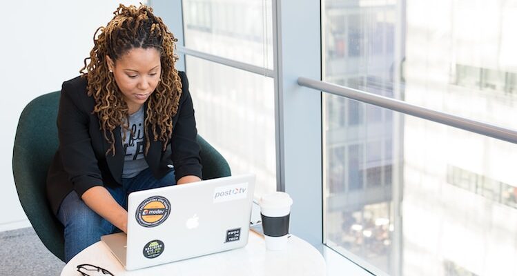 woman sits on padded chair while using MacBook during daytime