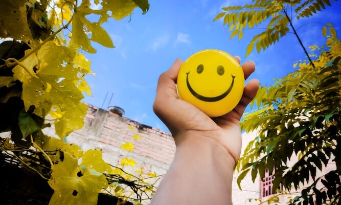 a hand holding a yellow smiley face ball